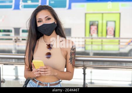 Femme avec un masque facial utilisant un téléphone portable en étant debout plate-forme Banque D'Images