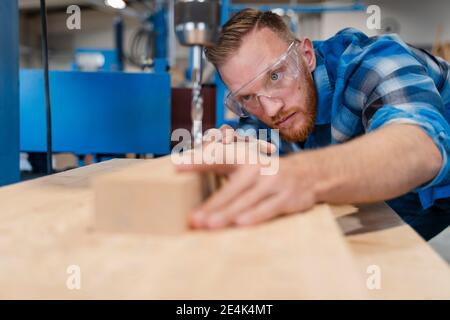 Portrait de menuisier portant des lunettes de protection, perçant une planche en bois Banque D'Images