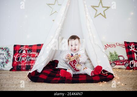 Petite fille mignonne jouant avec le jouet tout en étant assis dans une tente À la maison pendant Noël Banque D'Images