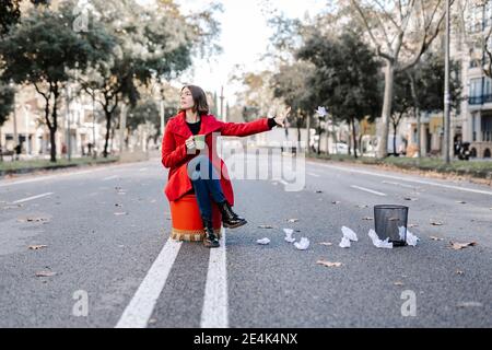 Jeune femme en blouson d'hiver avec une tasse de café à jeter froissés le papier est vide dans la poubelle sur la route Banque D'Images