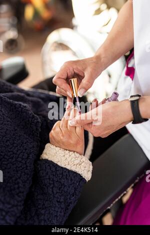 Mains de l'infirmière de sexe féminin appliquant du vernis à ongles à la femme handicapée à maison de soins Banque D'Images