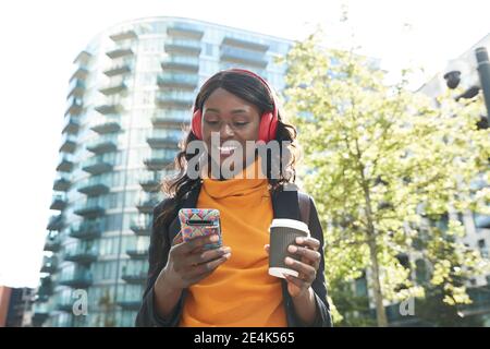 Femme souriante professionnelle avec une tasse de café jetable écoutant de la musique à parc de bureaux Banque D'Images