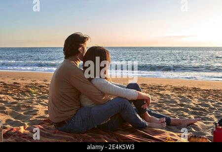 Jeune couple regardant la vue sur la mer tout en étant assis sur la plage Banque D'Images