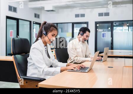 Jeune opérateur asiatique femme agent avec des micro-casques et des collègues travaillant service client dans un centre d'appels Banque D'Images