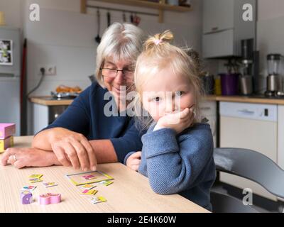 Une fille blonde bouleversée assise par une grand-mère jouant au puzzle au restaurant table dans la cuisine Banque D'Images