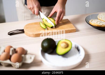 Mains de la femme coupant l'avocat sur la planche à découper Banque D'Images