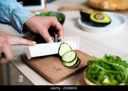 Mains de la femme qui coupe le concombre sur la planche à découper Banque D'Images