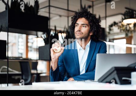 Jeune homme entrepreneur attentionné regardant loin tout en pressant le ballon de stress au bureau Banque D'Images