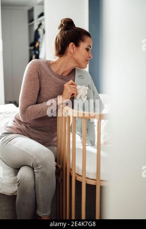 Femme adulte avec jouet éléphant imaginant tout en regardant le lit de bébé dans la chambre Banque D'Images