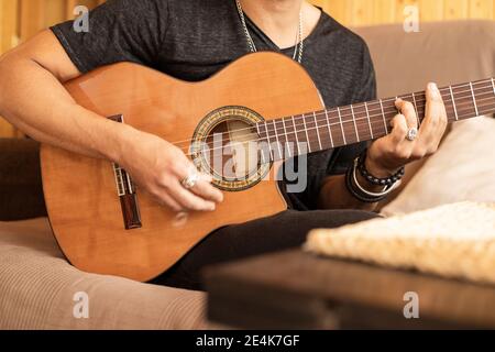 Homme jouant de la guitare acoustique tout en étant assis à la maison Banque D'Images