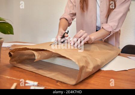 Femme artiste coupant du papier brun tout en préparant le paquet à la réception dans la salle de séjour Banque D'Images