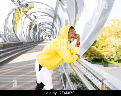 Homme d'affaires attentionné portant une chemise à capuchon jaune, penchée sur les balustrades de la passerelle Banque D'Images