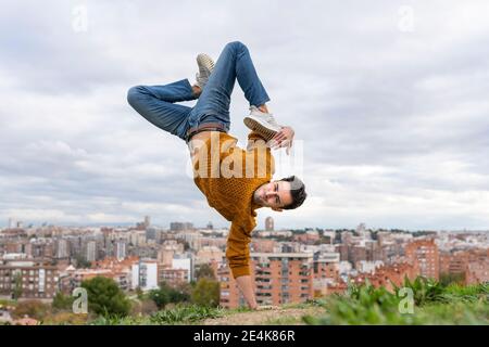 Jeune homme flexible faisant la main sur la colline dans la ville contre ciel Banque D'Images