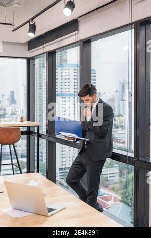 Un homme d'affaires caucasien intelligent qui se tient avec l'analyse de documents financiers dans moderne bureau dans le quartier des affaires Banque D'Images