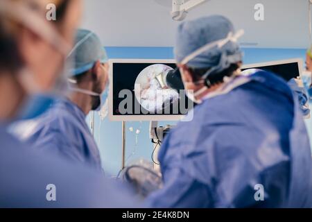 Professionnels qui surveillent la chirurgie sur écran d'ordinateur tout en étant debout chambre Banque D'Images