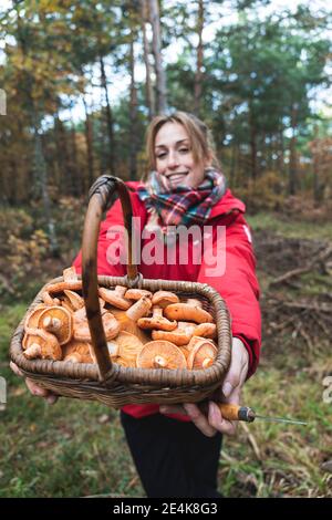 Femme souriante montrant un panier rempli de champignons dans la forêt automne Banque D'Images