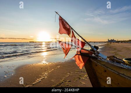 Allemagne, Mecklembourg-Poméranie occidentale, Ahlbeck, drapeaux rouges sur le bateau de pêche laissé sur la plage côtière sablonneuse au lever du soleil Banque D'Images