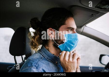 Jeune homme élégant qui règle le masque de protection en voiture Banque D'Images