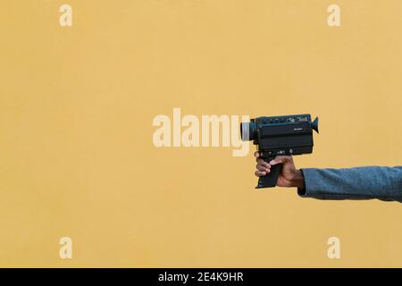 Homme tenant un appareil photo des années 1980 contre un mur jaune Banque D'Images