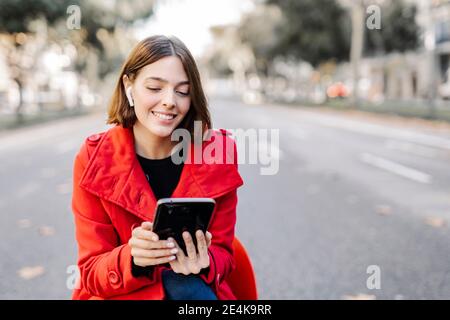 Souriante femme tendance utilisant une tablette numérique tout en écoutant de la musique asseyez-vous sur la route Banque D'Images