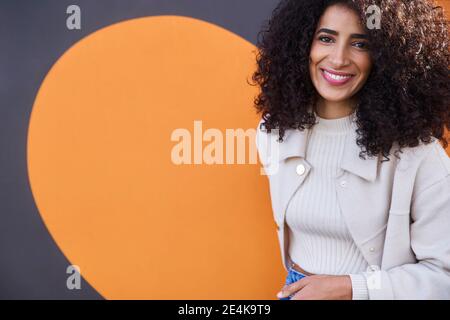 Belle femme souriante avec des cheveux bouclés debout contre le mur Banque D'Images