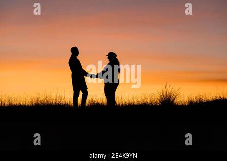 Dans la silhouette de l'homme et de la femme tenant les mains en se tenant debout contre le ciel Banque D'Images