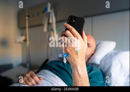 Un patient de sexe masculin utilisant un téléphone portable en étant allongé sur le lit dans le service hospitalier Banque D'Images