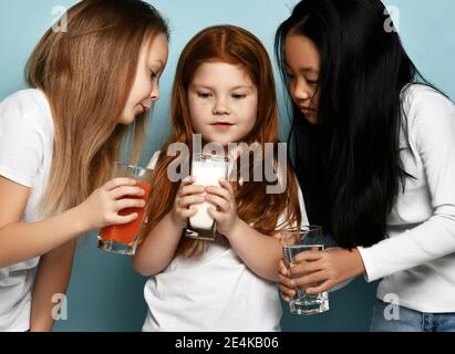 Filles de course mixte amis en jeans et t-shirts blancs debout avec des verres d'eau, de lait et de jus et regardant le lait Banque D'Images
