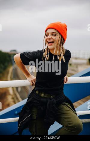 Jeune femme joyeuse debout sur une rampe sur le pont contre le ciel Banque D'Images