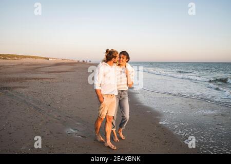 Un jeune couple marche à la plage contre un ciel dégagé pendant les vacances Banque D'Images