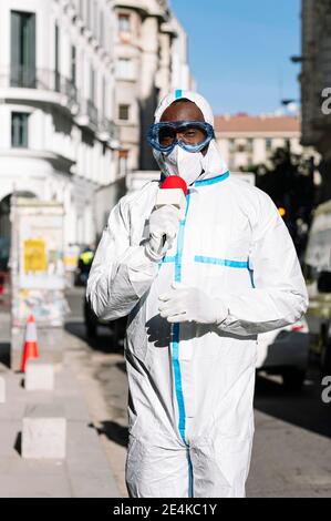 Un journaliste masculin portant un costume de protection parlant au-dessus d'un microphone en position debout sur la rue Banque D'Images