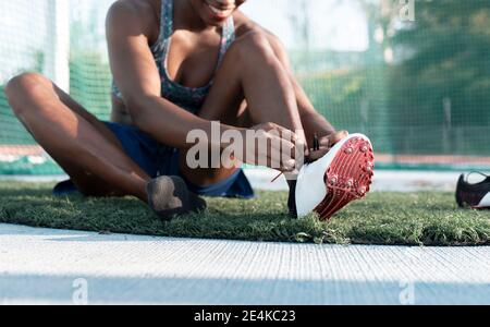 Une athlète féminine se noue avec une cordonneuse tout en se assis sur un terrain de sport contre net Banque D'Images