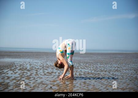 Femme mûre se pliant tout en pratiquant le yoga à la plage contre le ciel Banque D'Images