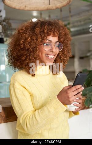 Femme souriante utilisant un smartphone dans un café Banque D'Images