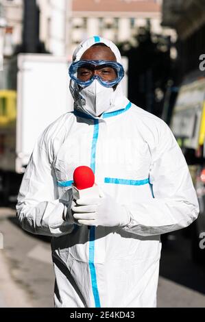 Un journaliste masculin portant un costume de protection avec microphone debout dans la rue Banque D'Images