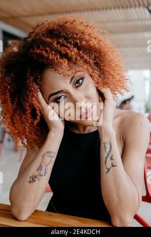 Femme adulte de taille moyenne confiante avec tatouage se penchant sur la table à l'intérieur café Banque D'Images