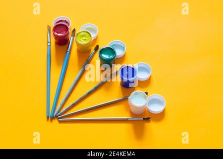 Les brosses et les bocaux de gouache sont disposés sur un arrière-plan jaune Banque D'Images
