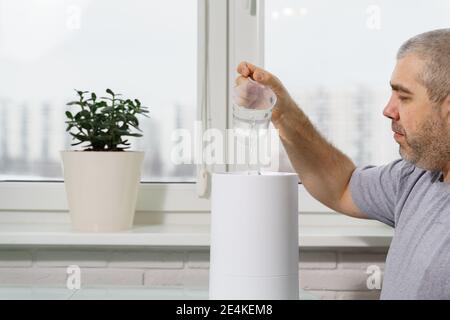 l'homme verse de l'eau dans un réservoir d'humidificateur en utilisant un humidificateur à la maison Banque D'Images