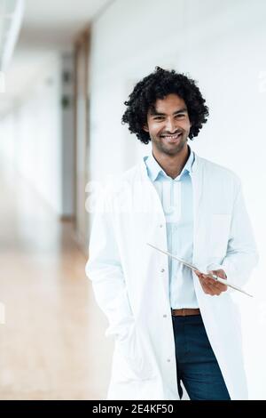 Jeune homme souriant, un professionnel de la santé tient une planchette à pince tout en se tenant debout couloir de l'hôpital Banque D'Images