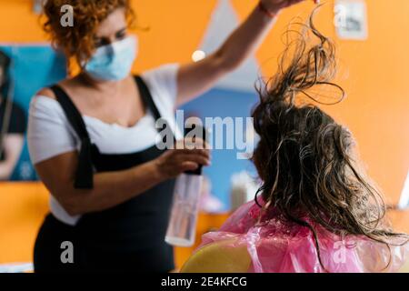 Coiffeuse féminine vaporisant de l'eau sur les cheveux bruns de la fille à barber boutique Banque D'Images