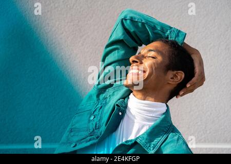 Homme souriant en se tenant les yeux fermés contre multicolore mur Banque D'Images