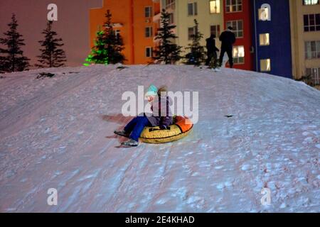 Enfant s'amusant sur le tube de neige portant un masque médical pendant le coronavirus COVID-19. Le garçon fait du tubing. Amusement d'hiver pour les enfants Banque D'Images