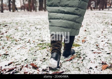 Gros plan des chaussures d'hiver pour femme. Femme marchant dans un parc enneigé portant un long manteau chaud et de hautes bottes en daim vert Banque D'Images