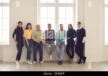 Une équipe de personnes gaies et variées se tenant près de la fenêtre, souriant et regardant l'appareil photo Banque D'Images