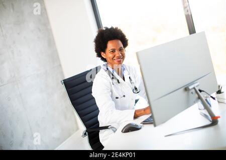 Femme afro-américaine médecin portant un manteau blanc avec stéthoscope assis derrière le bureau Banque D'Images