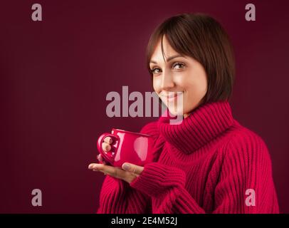 une fille avec un petit bob dans un chandail rouge s'assoit avec une tasse de thé ou de café, isoler Banque D'Images