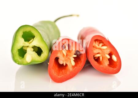 Trois poivrons chauds mûrs frais et épicés, rouges et verts, sur fond blanc. Au premier plan, au foyer, macro, tranches de trois poivrons. Banque D'Images