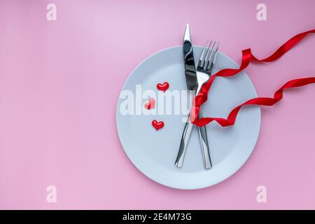 Table romantique. Assiette, fourchette et couteaux avec ruban sur fond rose. Pour bannière. Le concept de la Saint-Valentin. Vue du dessus, espace copie Banque D'Images