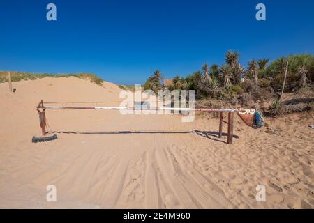 Barrière métallique ancienne blanche et rouge fermée sur une piste de sable à Trafalgar Cape, village de Canos Meca (Barbate, Cadix, Andalousie, Espagne) Banque D'Images