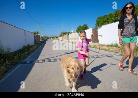 Petite fille de quatre ans marchant un chien à côté de la femme, sa mère, au milieu d'une rue dans le village de Vejer, Cadix, Andalousie, Espagne Banque D'Images